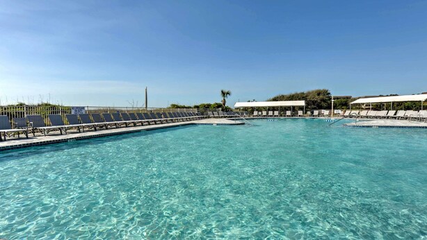 Une piscine d’eau cristalline, bordée de chaises longues et surveillée par un sauveteur.