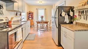 A kitchen with a central island, wooden chairs, a dining table, and a refrigerator with hanging oven mitts. - Penn Yan House Rental - Close to Wineries! (Penn Yan)