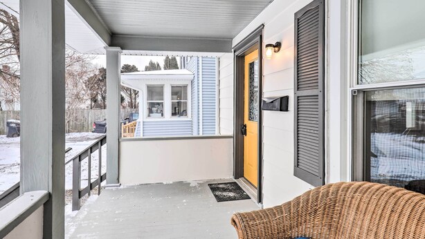 A covered porch with a wicker chair, a yellow door, and a view of a house in the background. - Penn Yan House Rental - Close to Wineries! (Penn Yan)