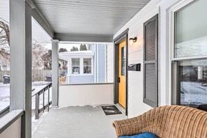 A covered porch with a wicker chair, a yellow door, and a view of a house in the background. - Penn Yan House Rental - Close to Wineries! (Penn Yan)