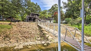 A wooden bridge over a rocky riverbank leading to a building with a staircase. - Dock, Deck & Boat Slip: Lakefront Eucha Home (Eucha)