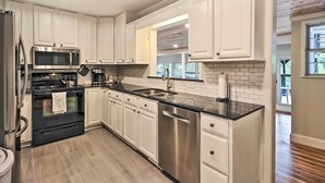 A modern kitchen with white cabinets, stainless steel appliances, and a black countertop. - Dock, Deck & Boat Slip: Lakefront Eucha Home (Eucha)