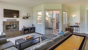 Een woonkamer met een flatscreen televisie, een open haard, een pooltafel en een bank.