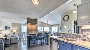 A spacious kitchen with a brick accent wall, a dining area with a sofa and chairs, and a large clock on the wall. - Westbrook Home w/ Ocean Views - Walk to Beach (Westbrook)