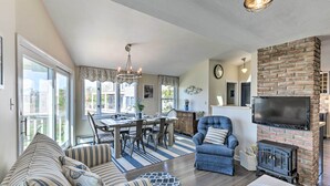 A spacious living room with a fireplace, a dining area, and a large window overlooking a cityscape. - Westbrook Home w/ Ocean Views - Walk to Beach (Westbrook)