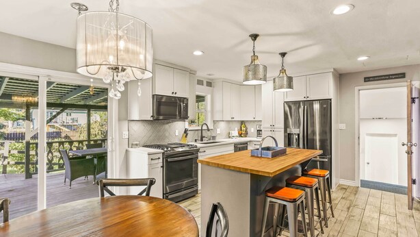 A modern kitchen with stainless steel appliances, a wooden dining table, and a bar area with stools. - Spacious Family Home w/ Garage Game Room & Office! (Boise)