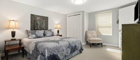 Un dormitorio con cama, dos mesitas de noche con lámparas, una silla, un armario y una puerta.