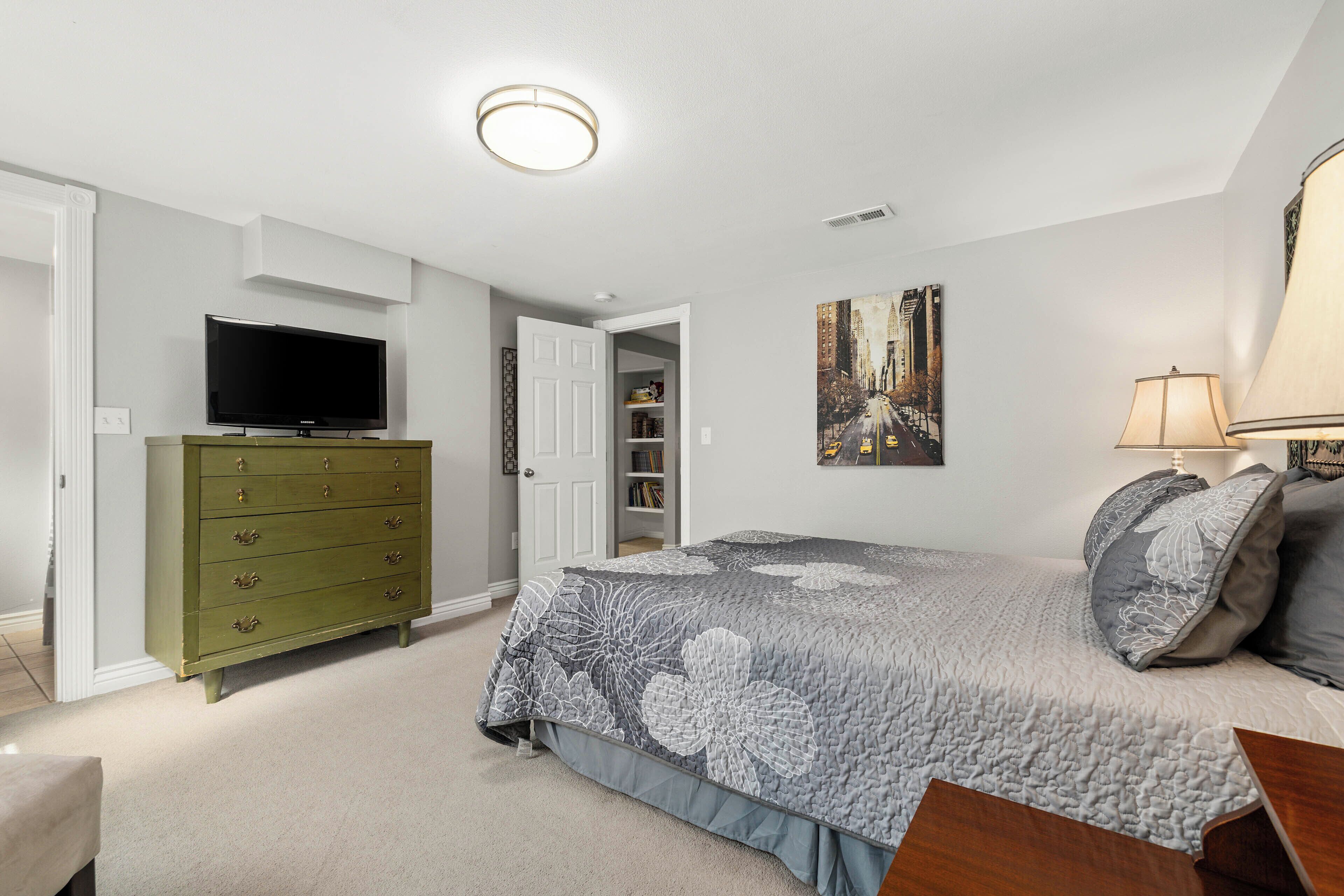 A bedroom with a bed, dresser, television, and artwork on the wall.