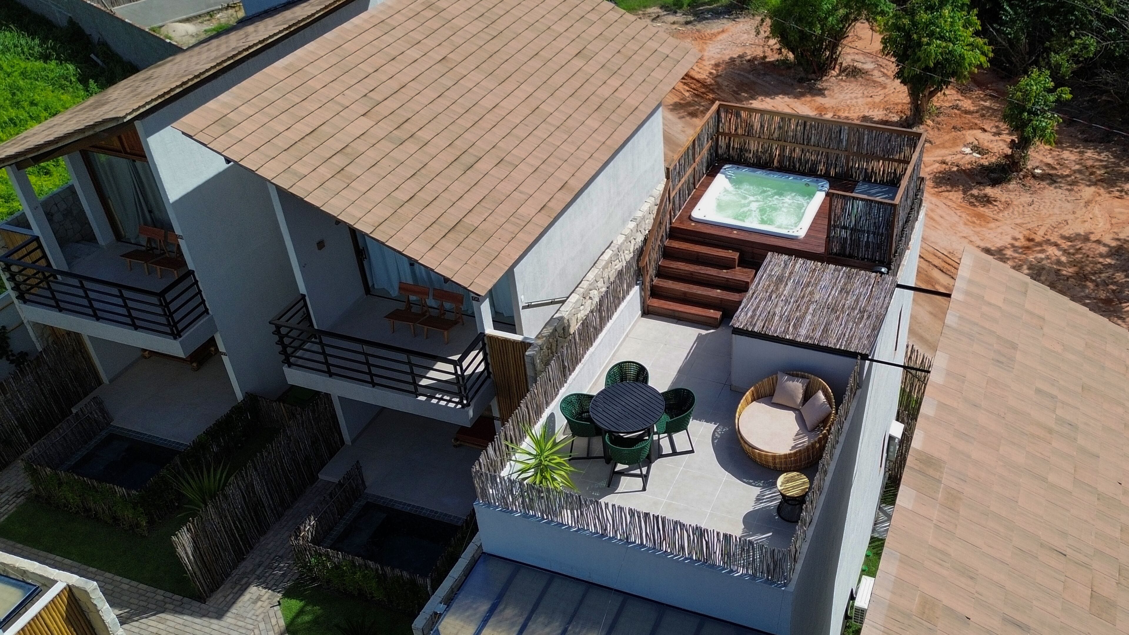 A modern two-story house with a rooftop patio featuring a hot tub, outdoor seating, and a small garden area.