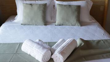 Una cama bien tendida con sábanas blancas, dos almohadas verdes y dos toallas blancas enrolladas.