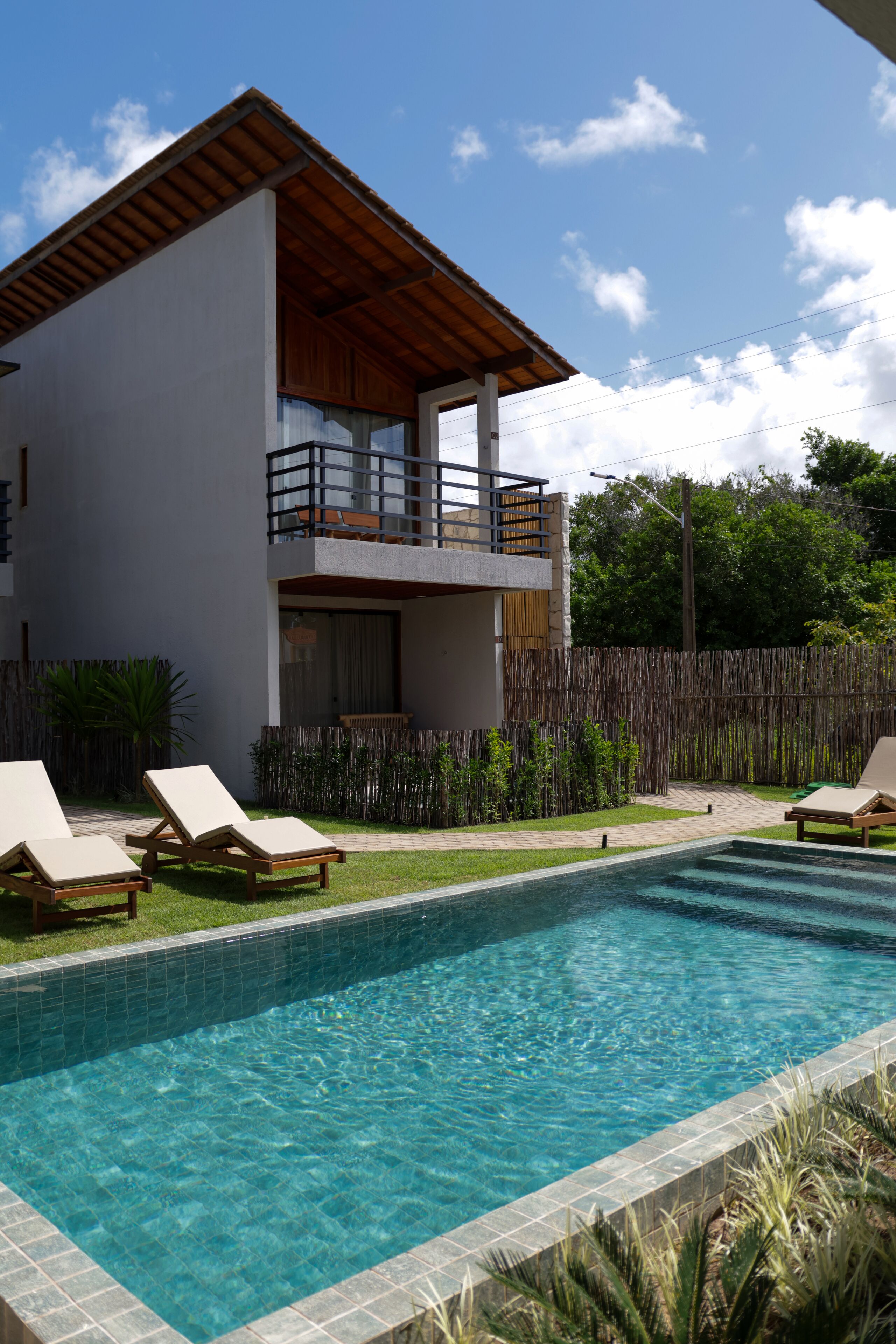 Uma casa moderna de dois andares com piscina, espreguiçadeiras e um deck de madeira.
