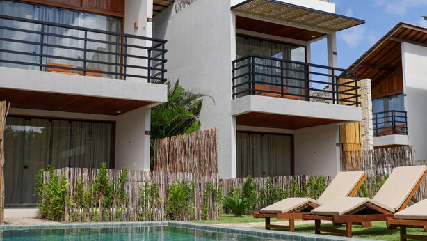 Un hotel moderno con piscina, varios balcones y sillones de descanso.