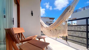 Una silla de lounge de madera y una mesa en un balcón con una hamaca.