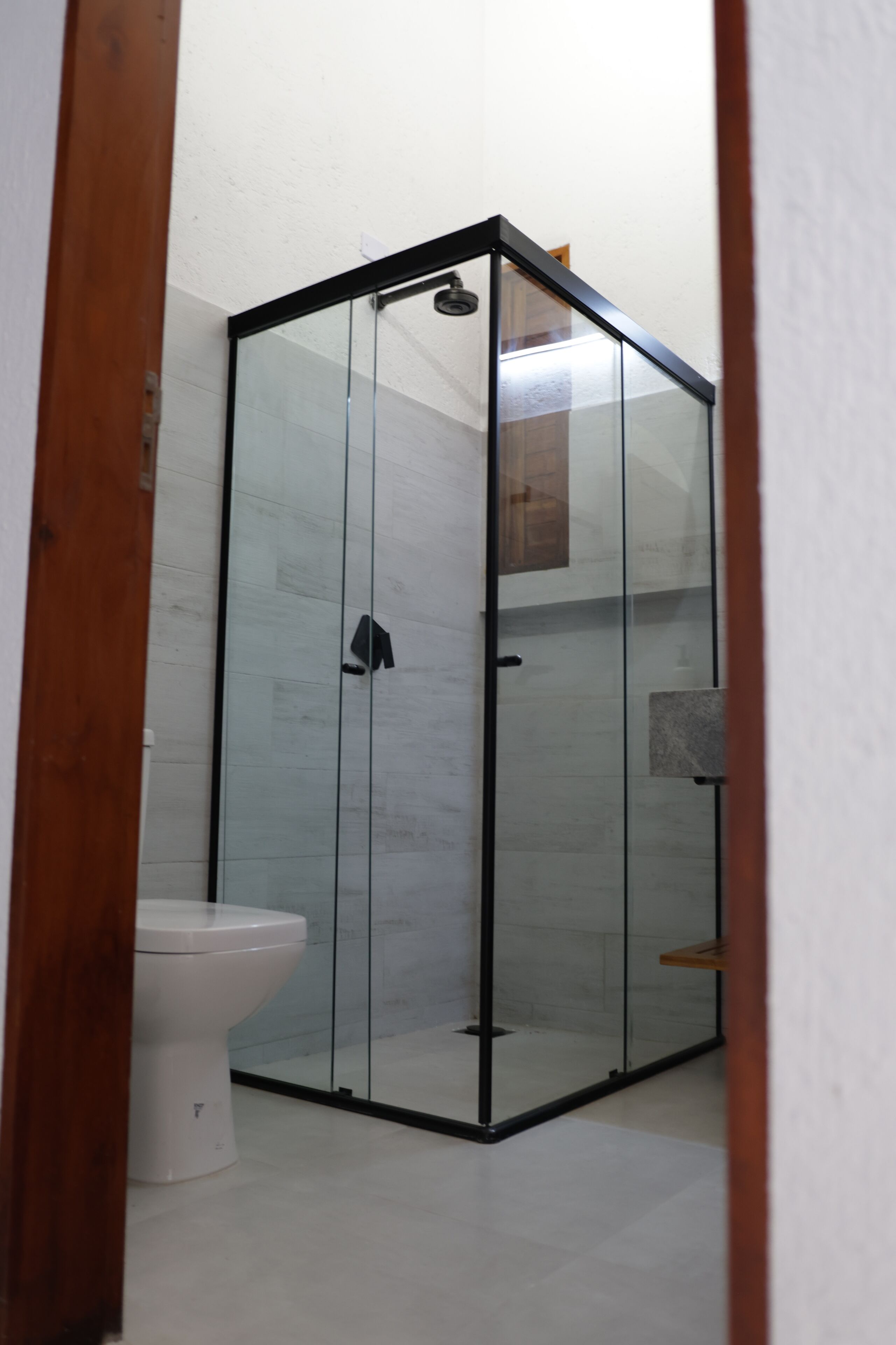 A modern bathroom with a glass-enclosed shower, a white toilet, and a wooden door frame.