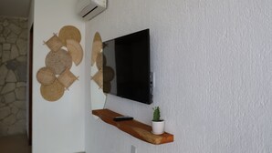 Una sala de estar moderna con un televisor de pantalla plana montado en una pared texturizada, un estante de madera con una planta en maceta y un control remoto.