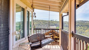 Ein Balkon mit Schaukelstuhl, einem kleinen Tisch und Blick auf eine hügelige Landschaft.