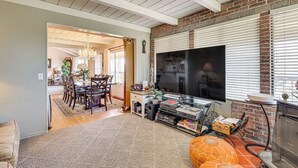 Ein Wohnzimmer mit Fernseher, Kamin, Essbereich und einer durchgehenden Tür erkennbaren Küche.