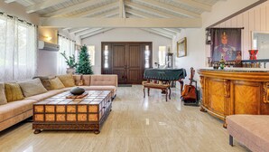 Ein geräumiges Wohnzimmer mit hohen Decken, einem Holztisch, einer Couch, einem Klavier und einem großen Holzschrank.