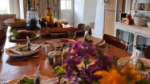 A dining room with a wooden table set for a meal, a chandelier, and a rustic kitchen in the background.