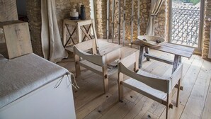 A rustic stone-walled room with wooden furniture, a small table with a basket, and a view through a window.