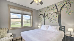 Un dormitorio con una cama grande, una ventana con vistas, un ventilador de techo y un mural de un árbol en la pared.