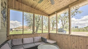 Un patio cubierto con zona de estar acolchada y una pequeña mesa, con amplias ventanas que ofrecen vistas al exterior.