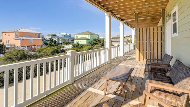 A wooden deck with a white railing, outdoor furniture, and a view of neighboring houses. - Emerald Isle Vacation Home: Walk to Beach! (Emerald Isle)