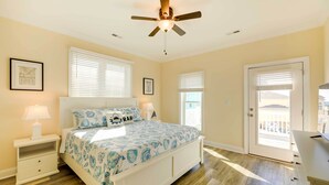 A bedroom with a bed, nightstands, a ceiling fan, and a door leading to a balcony. - Emerald Isle Vacation Home: Walk to Beach! (Emerald Isle)