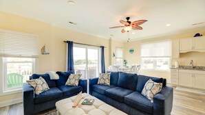 A living room with two dark blue sofas, a beige ottoman, and a ceiling fan. - Emerald Isle Vacation Home: Walk to Beach! (Emerald Isle)