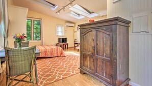Une pièce comprenant un lit, une armoire en bois, une chaise en osier, un téléviseur et une fenêtre avec des stores.