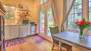 Une cuisine avec des meubles blancs, un four à micro-ondes et un coin repas comprenant une chaise en osier et un vase de fleurs.