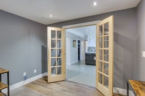 A spacious room with a large wooden door, a wooden table, and a visible kitchen area in the background. - Denver Vacation Home w/ Home Theater! (Denver)