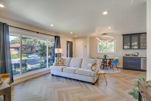 A spacious living area with a large window, a sofa, a dining table, and a kitchen area. - Denver Vacation Home w/ Home Theater! (Denver)