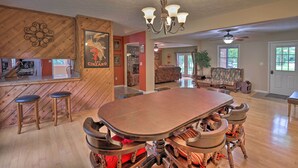 A spacious dining area with a large wooden table and bar stools, a chandelier, and a kitchen area visible in the background. - Hendersonville Home w/ Fire Pit: 5 Mi to Downtown! (Hendersonville)
