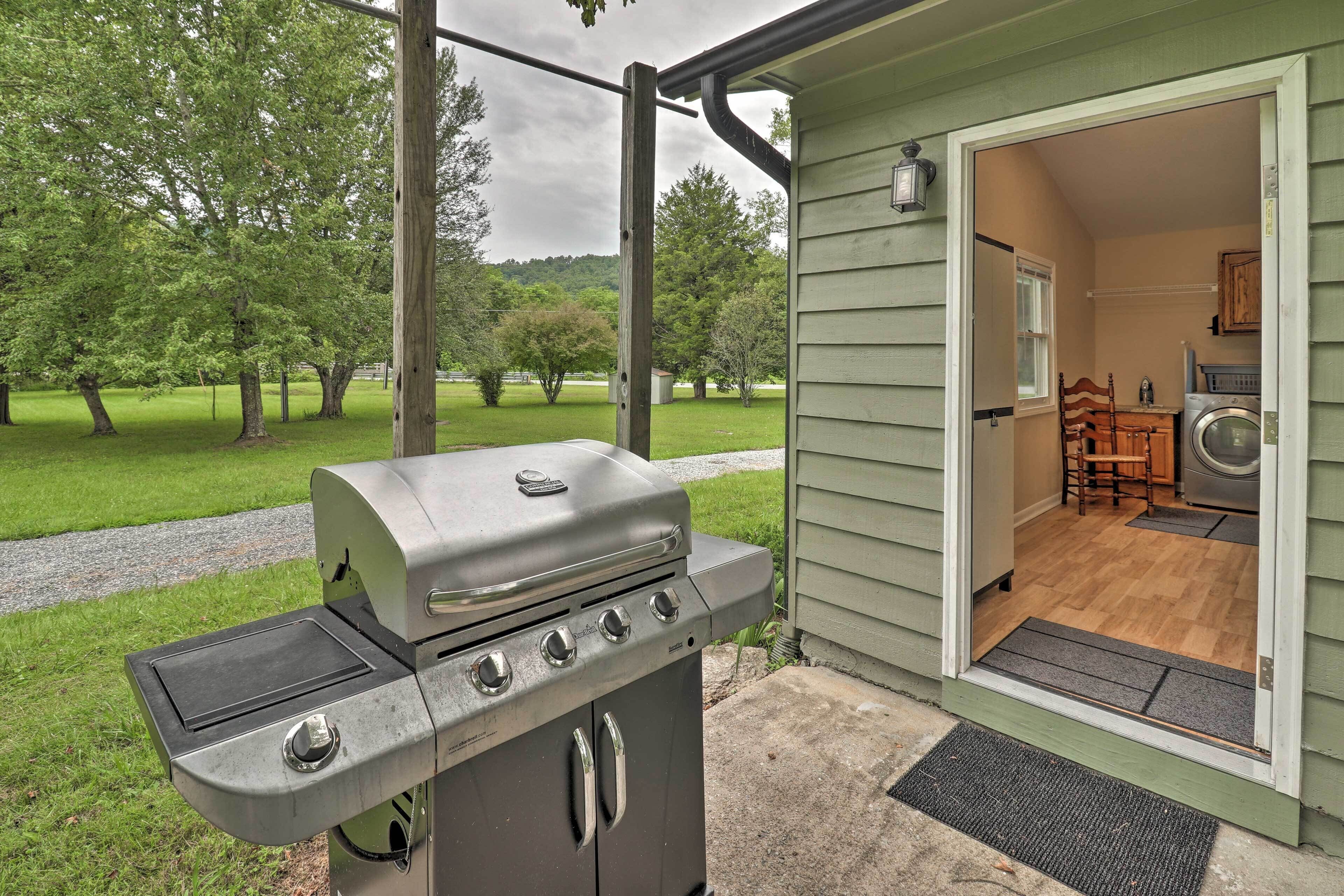 Une terrasse dotée d’un barbecue en acier inoxydable, d’une table en bois et d’une porte donnant sur une buanderie.