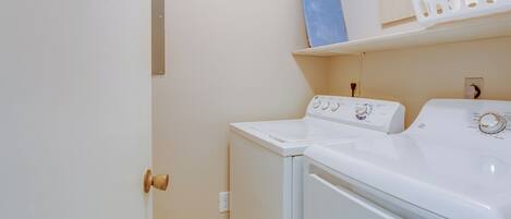 A laundry room with a front-loading washer and dryer, a wooden door, and a shelf above the dryer.
