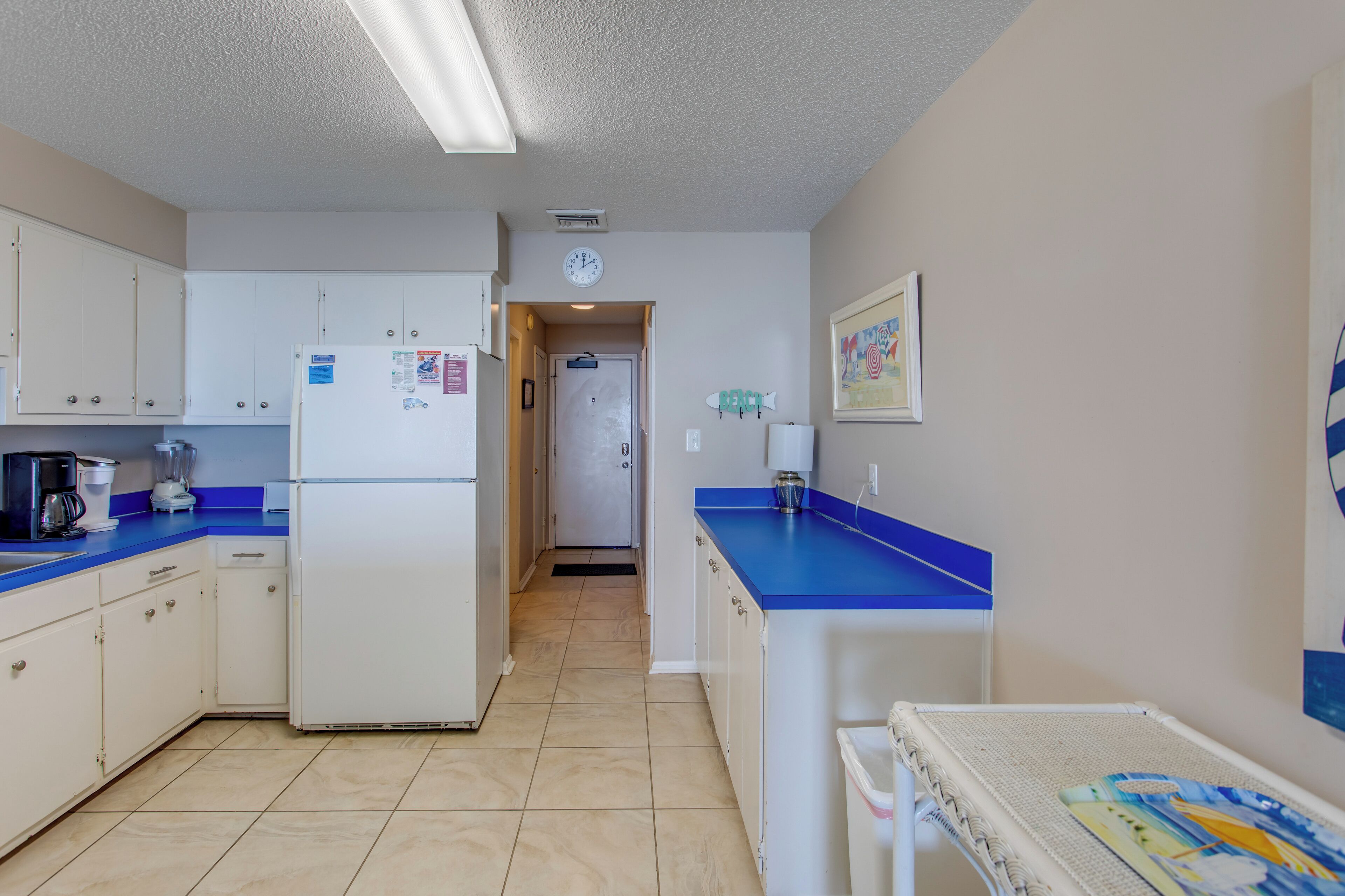 A kitchen with white cabinets, a blue countertop, a refrigerator, and a microwave.