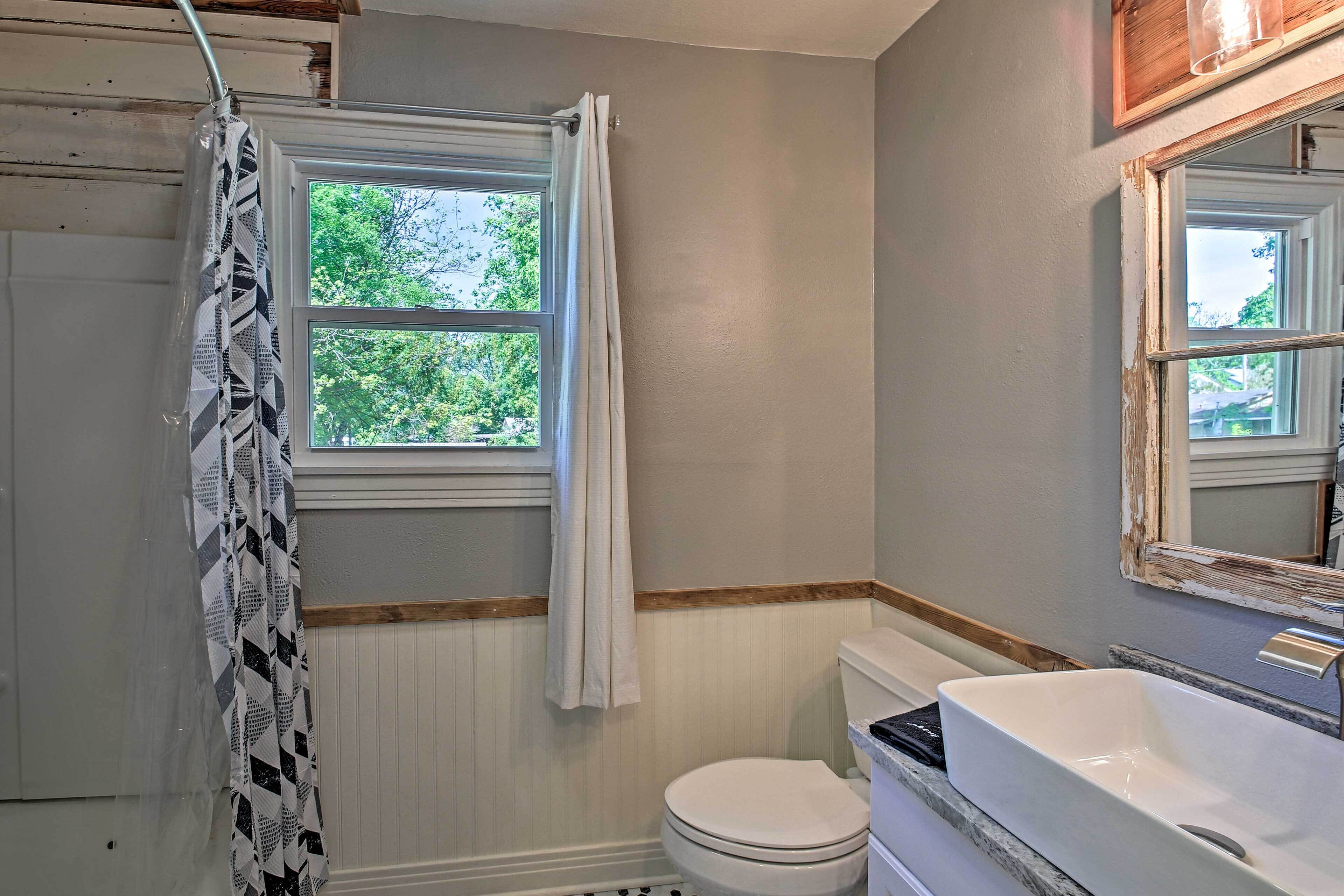 Un baño con inodoro y lavamanos blancos, y una ventana que da a vistas de vegetación.