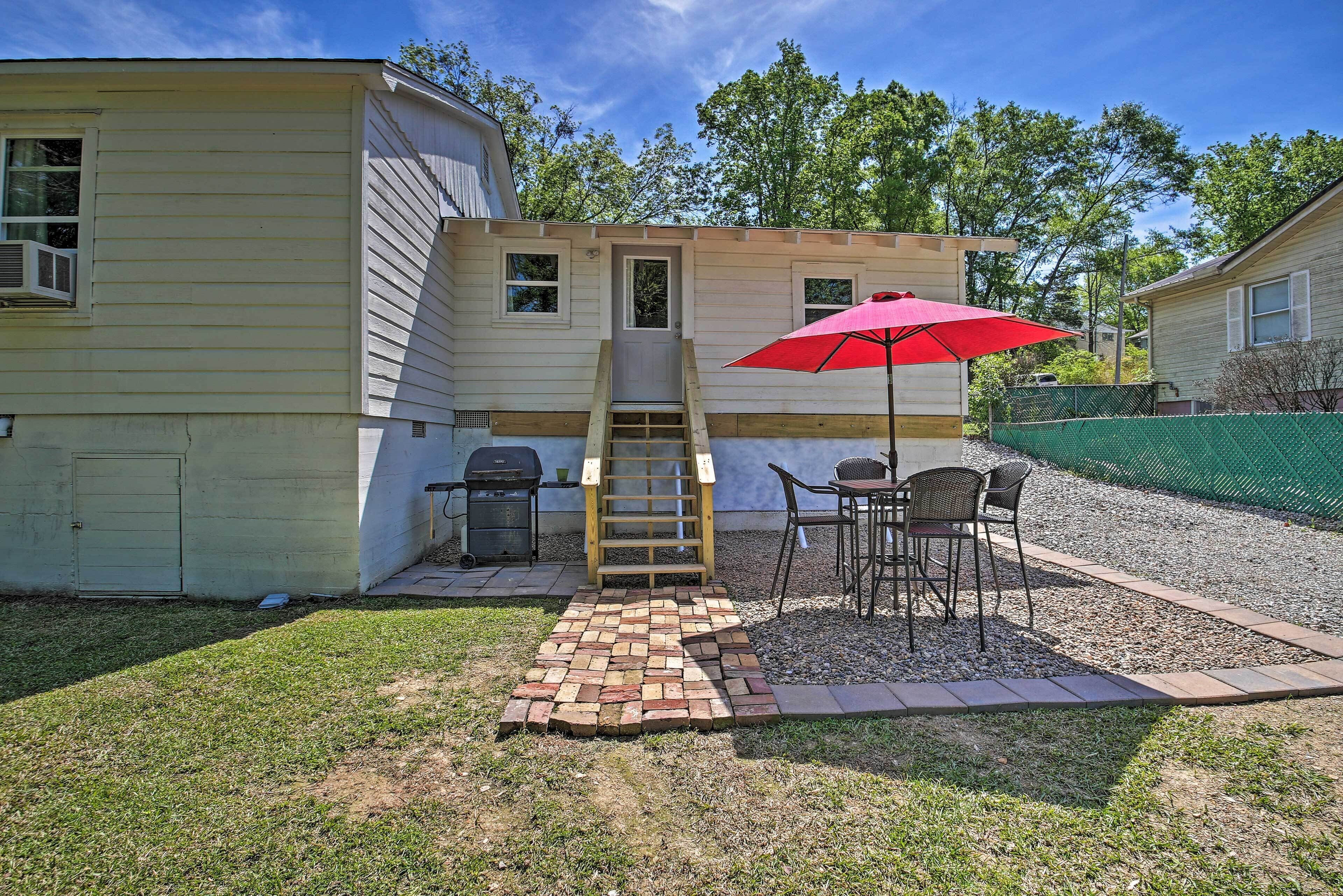 A small house with a wooden deck, a red umbrella, and a grill.