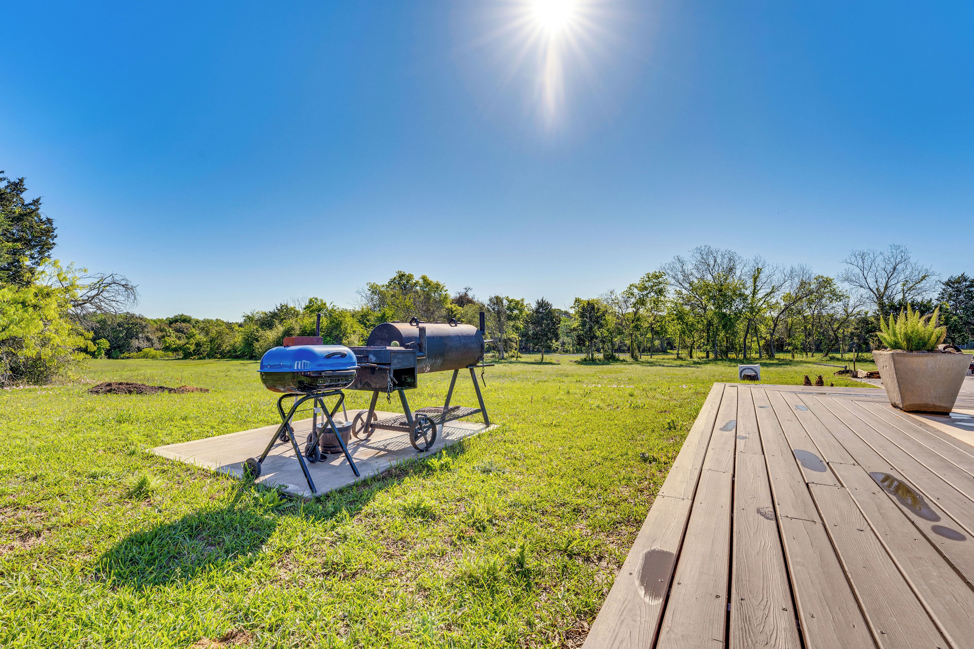 A wooden deck with a barbecue grill and a grill on a concrete pad in a grassy area.