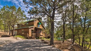 A wooden cabin with a green roof, surrounded by trees, and a paved driveway leading to the entrance. - Alto Home w/ Deck & Views ~ 15 Mi to Ski Apache! (Alto)