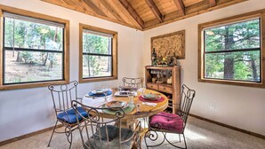 A dining area with a wooden table, metal chairs, and large windows offering views of trees. - Alto Home w/ Deck & Views ~ 15 Mi to Ski Apache! (Alto)