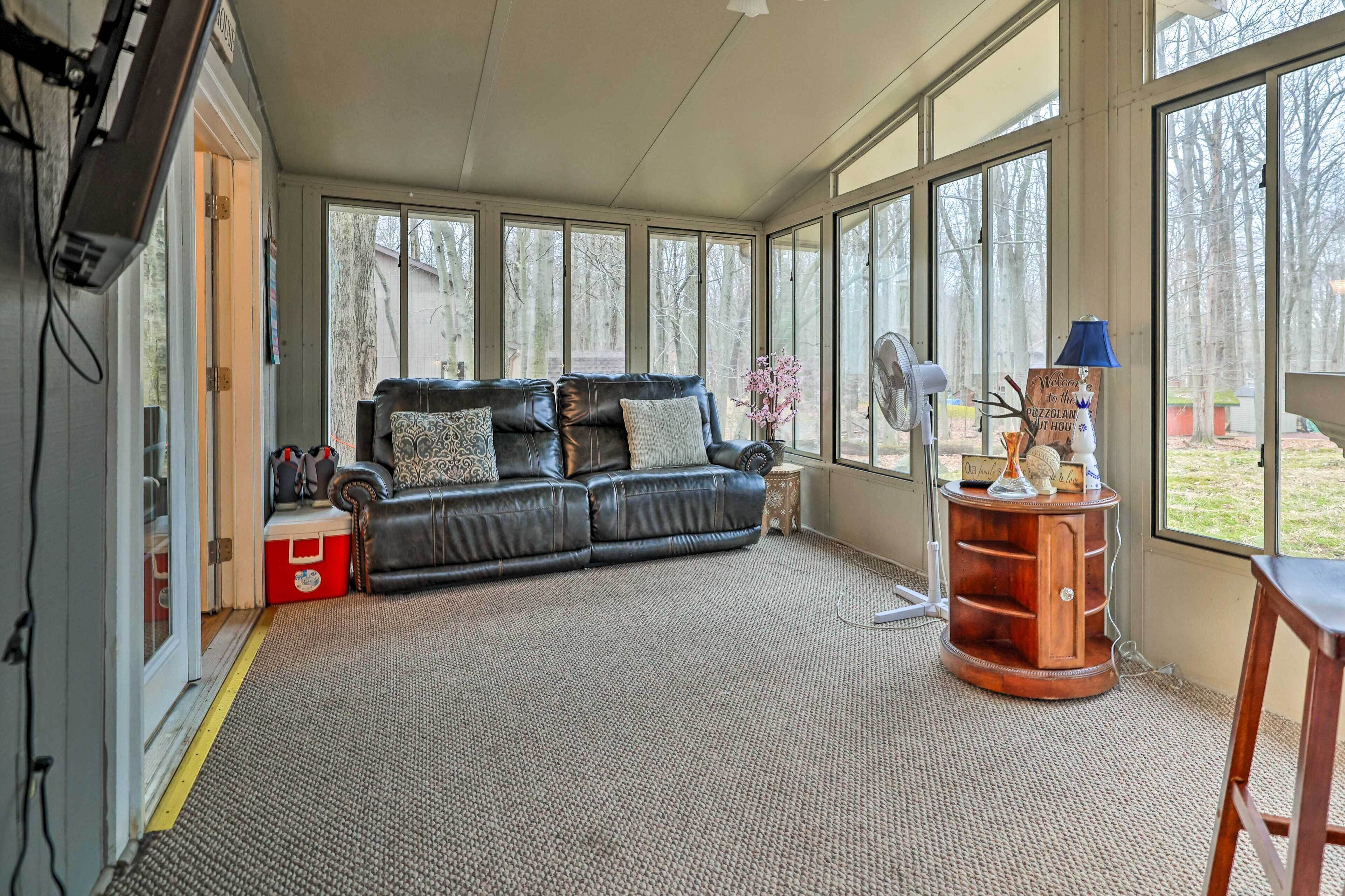 A living room with a black leather sofa, a wooden side table, and a large window with a view of trees.