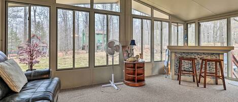 A sunroom with a large window, a fan, a wooden stool, and a couch.