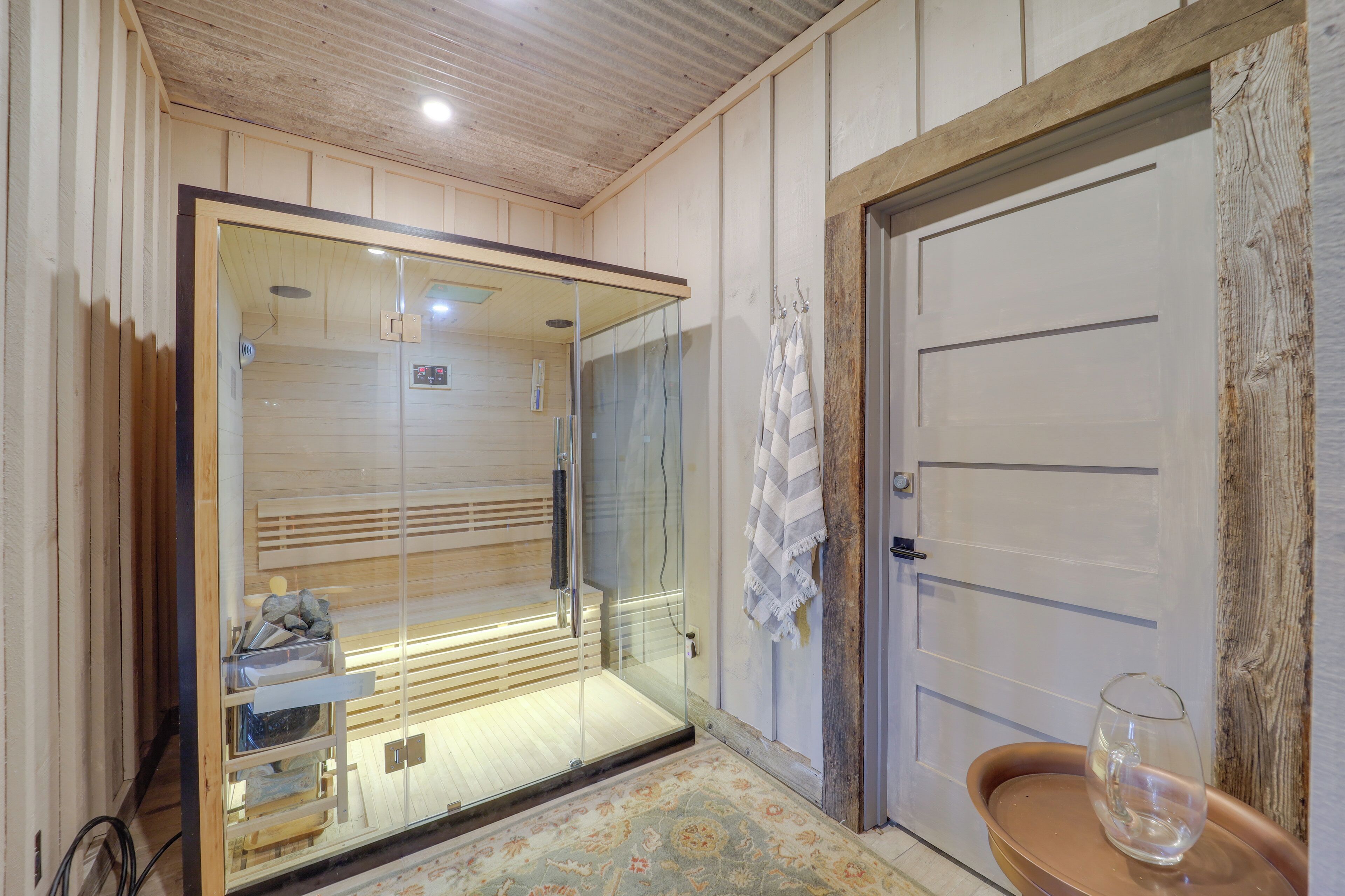 Una stanza con cabina doccia in vetro, una porta in legno e un tavolino con un bicchiere.