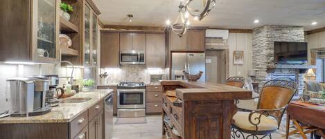A spacious kitchen with a central island, stainless steel appliances, and a stone fireplace.