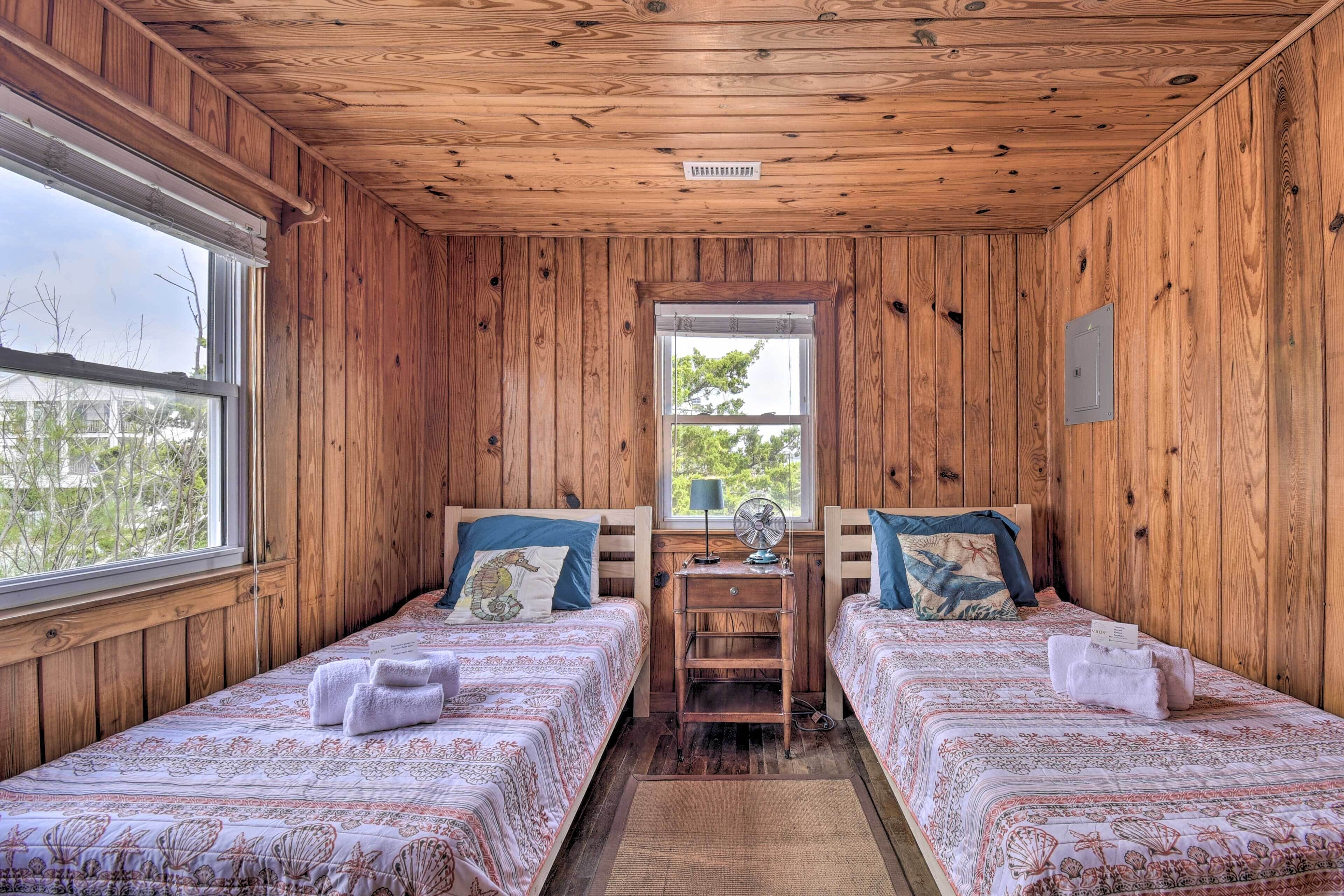Una habitación con paneles de madera, dos camas, una mesita y una ventana.