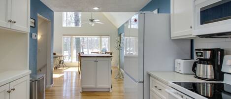 A modern kitchen with white cabinets, a stainless steel refrigerator, a black stove, and a coffee maker.