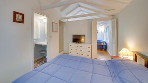 A bedroom with a bed, a dresser, a TV, and a bathroom visible through an open door. - Couples Getaway Near Beaches: Northport Cottage (Lincolnville)