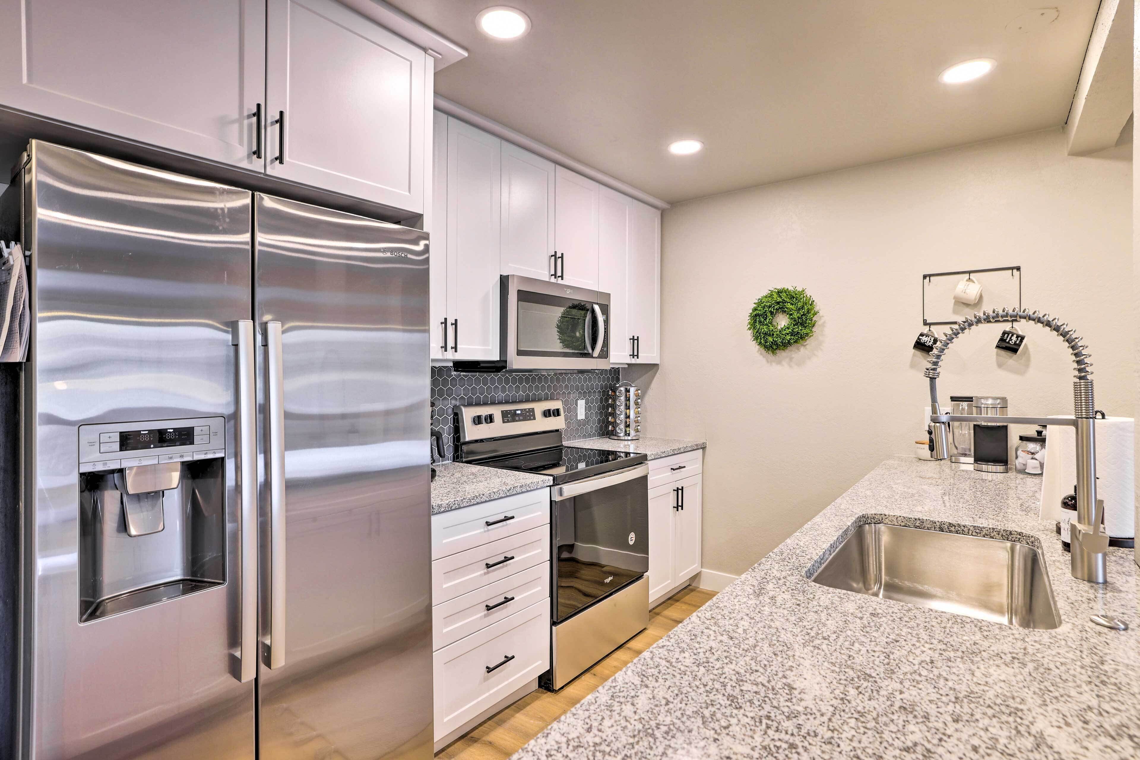 A modern kitchen with stainless steel appliances, white cabinetry, a granite countertop, and a stainless steel sink.